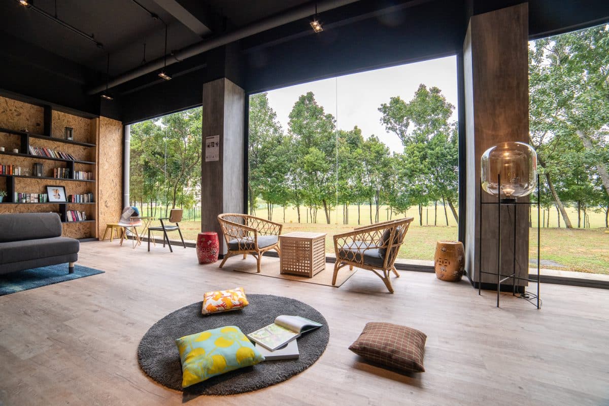 Coliwoo Boon Lay communal lounge with rattan armchairs, floor cushions, and floor-to-ceiling windows overlooking greenery