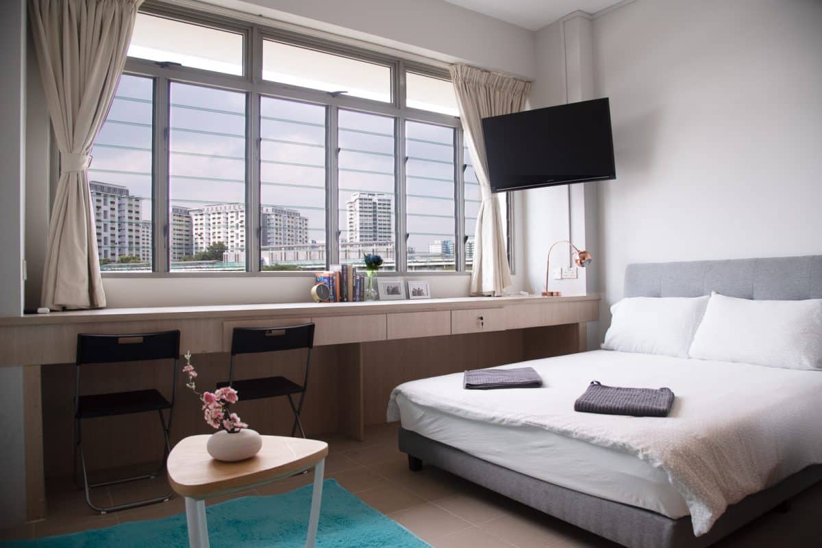 Queen Modified Suite bedroom at Coliwoo Boon Lay with queen-sized bed, wall-mounted TV, window-side workstation, and city view